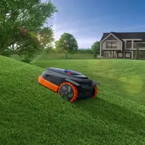 the Segway Navimow X315E Robotic Mower travelling up a steep lawn, with trees and a house in the background