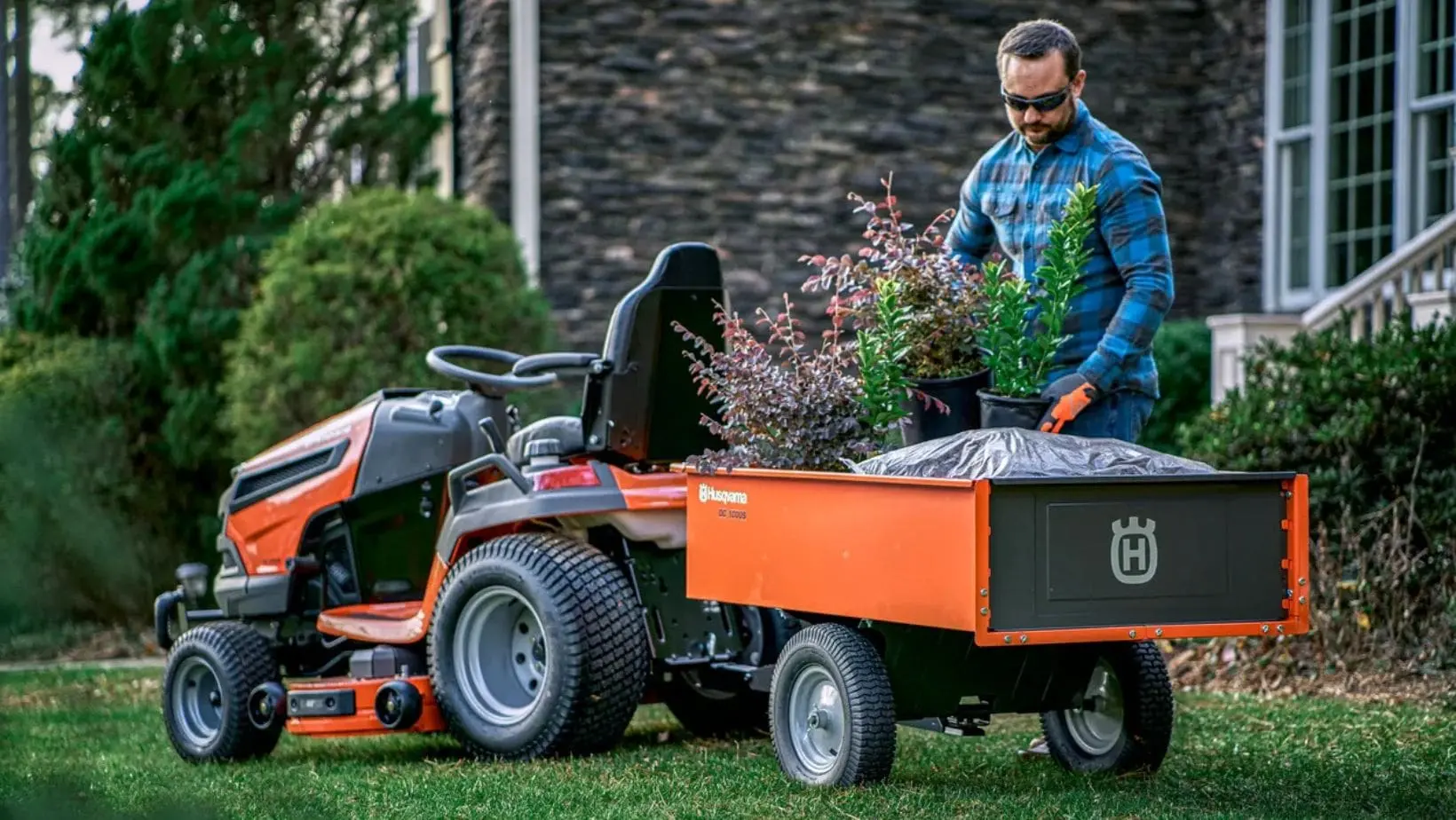 a man putting potted plants into a Husqvarna-branded trailer, which is attached to a Husqvarna riding mower