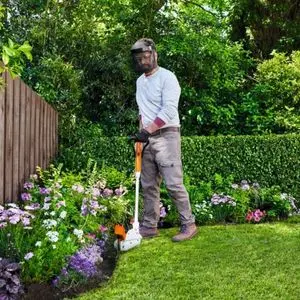 a man wearing visor and gloves, using the STIHL FSA 30 Cordless Grass Trimmer in a garden, where the lawns meets a flower bed