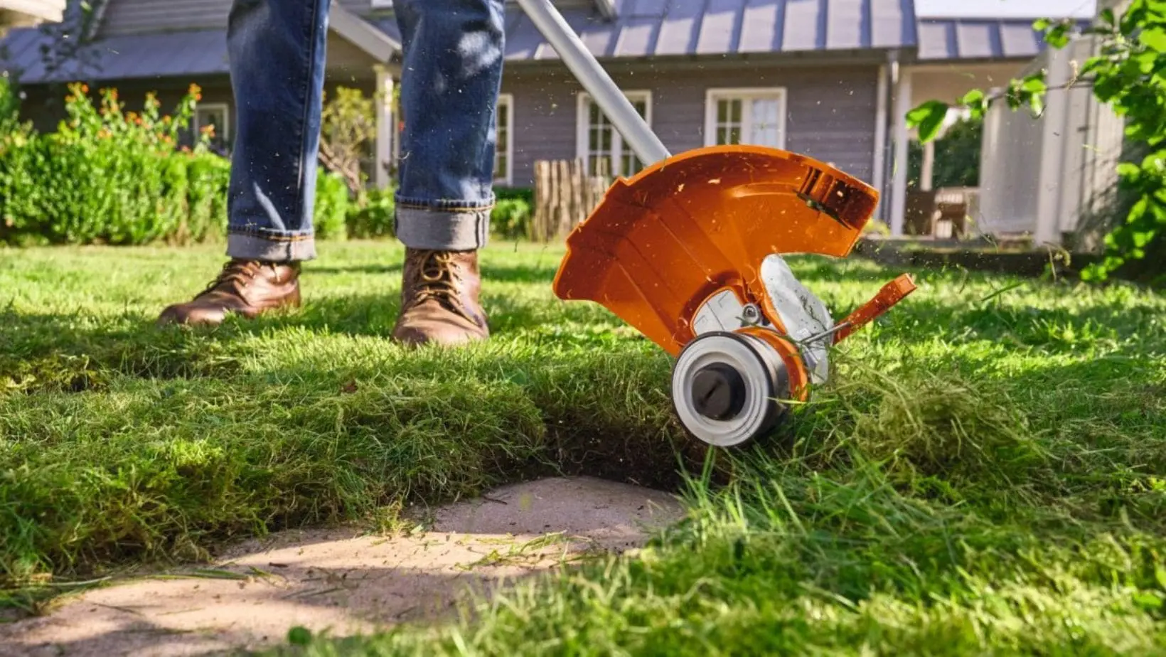 the underside of the STIHL FSA 50 Cordless Grass Trimmer as it cuts grass around slabs in a garden