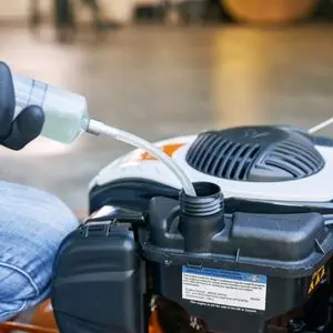 someone using a syphon to drain fuel from a STIHL petrol lawnmower's fuel tank