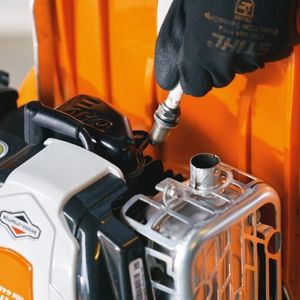 someone dressed in orange overalls and black gloves, removing the spark plug from a STIHL petrol lawn mower's engine