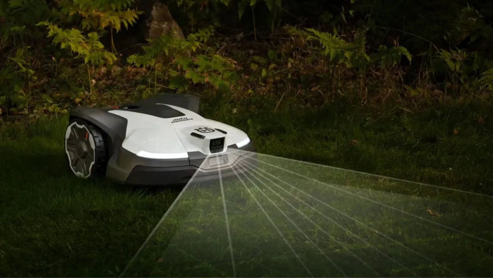 a white Husqvarna Automower, illuminated in a night-time garden, with a computer-generated graphic demonstrating its sensors' power