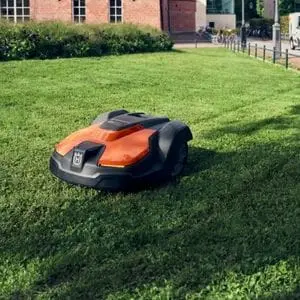 a Husqvarna Automower® 520 EPOS Robotic Mower on a large lawn, next to a street, with a red-brick building in the background