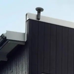 a Husqvarna EPOS™ RS1 Reference Station fixed to the top of a building with black cladding and a white-trimmed flat roof