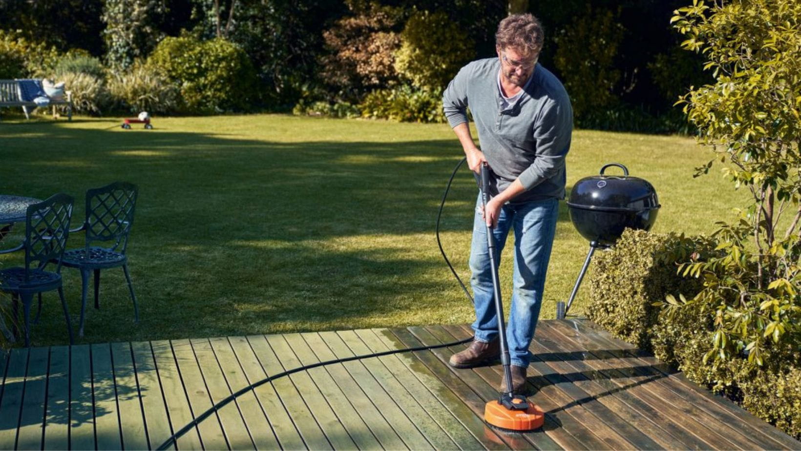 a man using a STIHL pressure washer with STIHL RA 110 Surface Cleaner attachment to clean decking in a garden