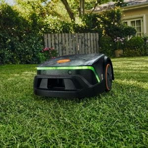 the STIHL iMOW® 4 EVO Robot Mower in a rural garden, with a house, fence, hedging and tree in the background
