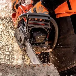 a close up of someone dressed in chainsaw PPE, using a Husqvarna chainsaw to cut a log