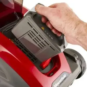 someone inserting a battery into a red Mountfield cordless mower