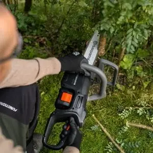 an overhead shot of a man using the Husqvarna Aspire™ C15X-P4A Chainsaw to cut a shrub's woody stem