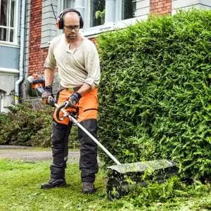a man using a Husqvarna multi tool with sweeper attachment to clear up garden debris near a hedge