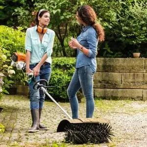 two women talking, one of whom is holding the STIHL KM 131 Petrol KombiEngine with bristle brush attachment