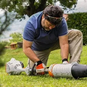 a man crouching on a lawn, attaching a blower attachment to the STIHL KM 56 RC-E Petrol KombiEngine