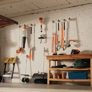 the STIHL KMA 80 R Cordless KombiMotor and 7 attachments, each neatly hanging from a white wall in a garage