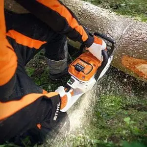 an overhead shot of someone dressed in black and orange chainsaw PPE, using the STIHL MSA 300 Cordless Chainsaw to cut a log