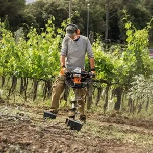 a man operating the STIHL BT 131 Petrol Earth Auger on sloping ground, in front of a row of saplings