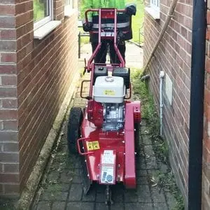 someone pushing the Camon SG30 Stump Grinder down a narrow passageway between redbrick houses