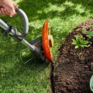 a close up of the Husqvarna 110iL FLXi Cordless Grass Trimmer cutting the edge of a lawn where it meets a flowerbed