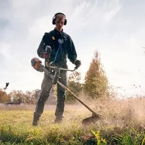 a man wearing ear defenders, operating the Husqvarna 535iRXT Brushcutter in a field