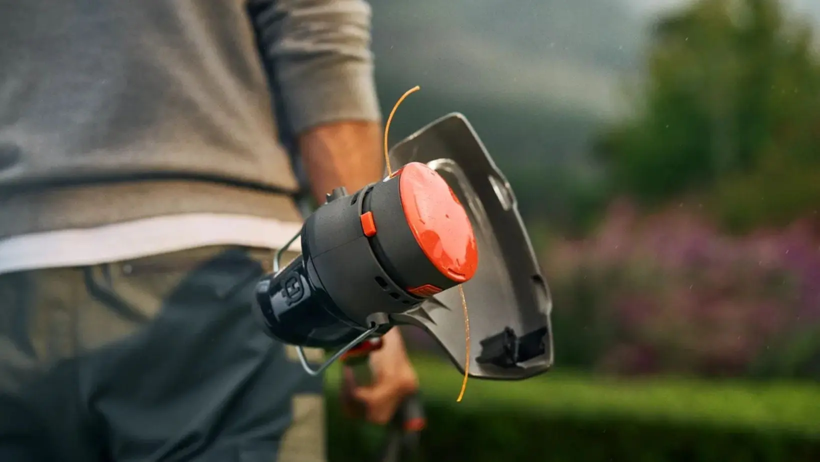 A man holding up the Husqvarna Aspire T28-P4A Battery Grass Trimmer to show the strimmer head