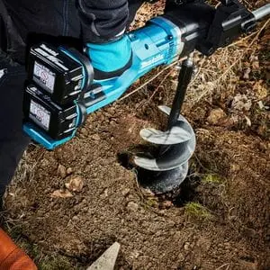 a close up of the Makita DDG460ZX7 Twin 18v LXT Earth Auger BL being used to drill a hole in soil
