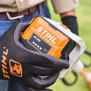 a close up of someone wearing black, STIHL-branded gloves, holding a STIHL AK 20 Battery