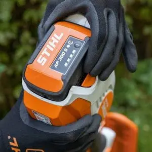 a close up of someone wearing black, STIHL-branded gloves, holding a STIHL AP 300 S Battery