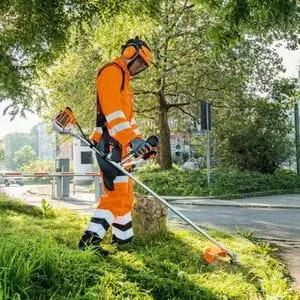 a man dressed in orange PPE, operating the STIHL FS 94 Petrol Brushcutter on a roadside verge