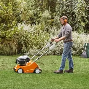 a man wearing ear defenders, pushing the STIHL RL 540 Petrol Scarifier across a lawn