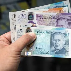 a close up of someone holding three £5 notes, one £20 note, and one £10 note
