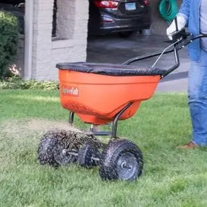 the Agri-Fab 45-0548 Pro Push Spreader dispensing seed on a lawn, outside a house