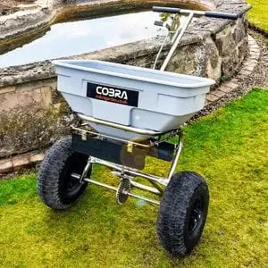 the Cobra HS60 Push Spreader on a lawn, next to a water feature