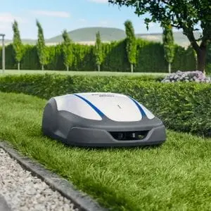 the Honda Miimo HRM 4000 LIVE Robotic Mower travelling across a narrow stretch of lawn between a hedge and gravel path