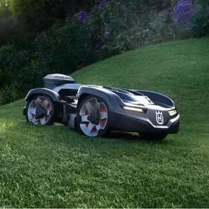 a Husqvarna Automower® 435X AWD NERA Robotic Mower travelling across an undulating lawn, with bedding plants in the background