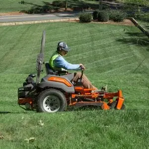 a man using the Husqvarna Z560X Zero Turn Mower to cut grass on an incline, near to a road