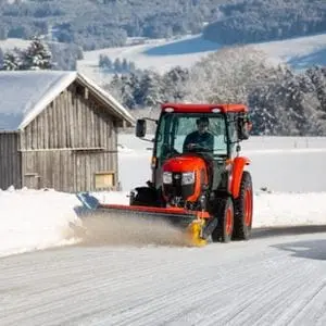 a Kubota compact tractor with snow plough attachment, clearing snow from a country road