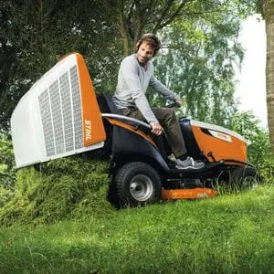 a man sat on the STIHL RT 6112 Petrol Ride-on Lawn Mower, dumping clippings from the collector onto the grass, in front of a tree