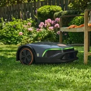 the STIHL iMOW® 5 EVO Robotic Mower mowing next to a wooden garden chair, with a flowerbed and picket fence in the background