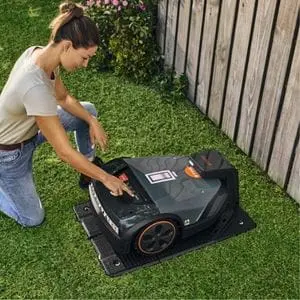 a woman knelt down, setting controls on a STIHL robot mower, which is sat in its charging station