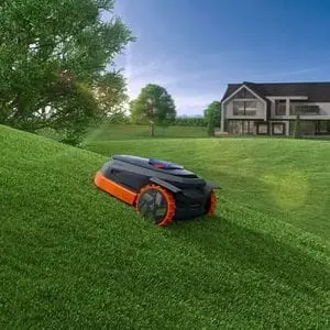 the Segway Navimow X350E Robotic Mower travelling up a steep lawn, with trees and a large house in the background
