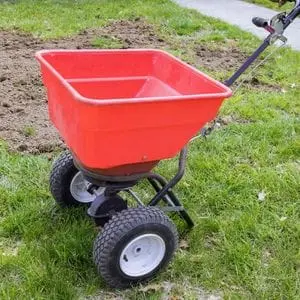 a red broadcast spreader on a patchy lawn