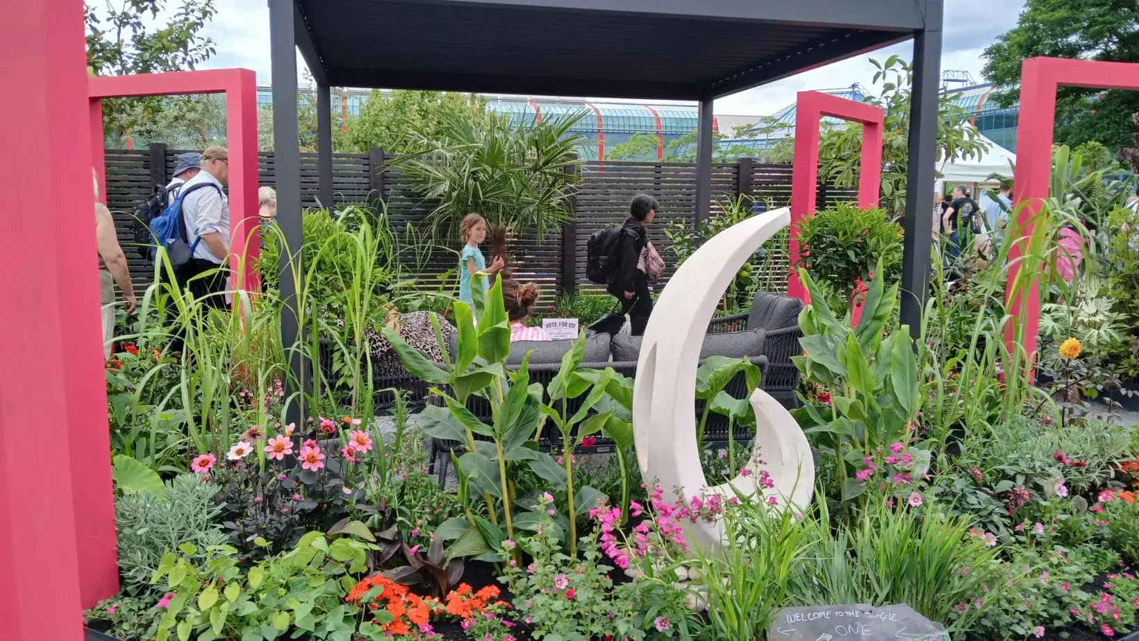 Dakic Garden Design's The Heart of the Jungle garden, featuring pink square arches, a grey gazebo, water feature, black slatted fence panels, and an extensive range of tropical plants