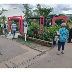 the entrance to Dakic Garden Design's The Heart of the Jungle garden at the NEC, with square, pink arches, a black-roofed gazebo, and extensive foliage prominent