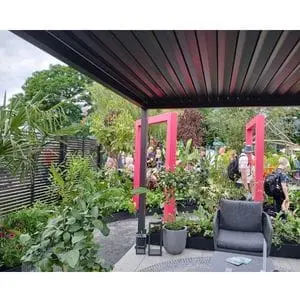 a view from the seated area underneath the black gazebo in Dakic Garden Design's The Heart of the Jungle garden, with square, pink arches; black, slatted fence panels; and the grey porcelain path particularly prominent