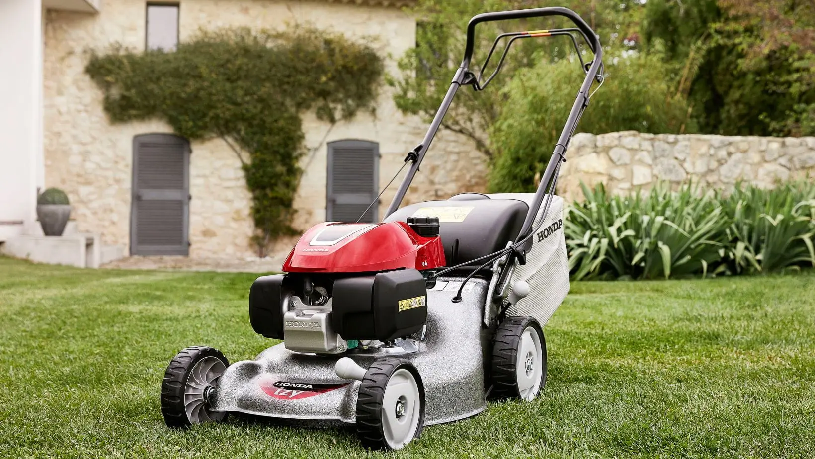 the Honda HRG466 Petrol Lawn Mower on a lawn outside a large country house, built from light-coloured brick