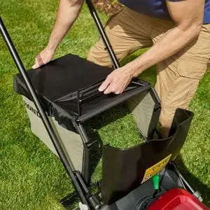 a man removing a grass box full of clippings from a red Honda lawn mower