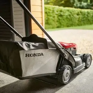 a Honda lawnmower next to an open garage door, looking out onto a garden