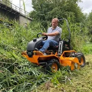 a man sat on the AS Motor AS 1040 YAK 4WD XL Ride-on Flail Mower, cutting very long grass and weeds near an underpass