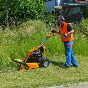 a man wearing a high-visibility jacket and ear defenders, using the AS-Motor AS 63 Brushcutter Mower to cut very long grass