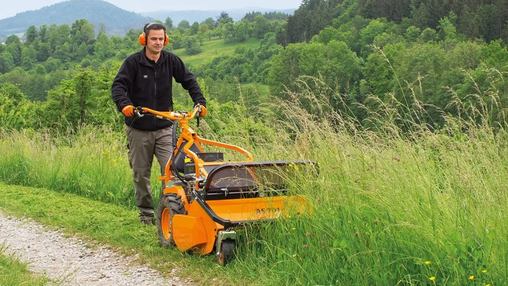 a man cutting long grass at the side of a countryside path, using the AS Motor AS 701 SM Walk-Behind Flail Mower